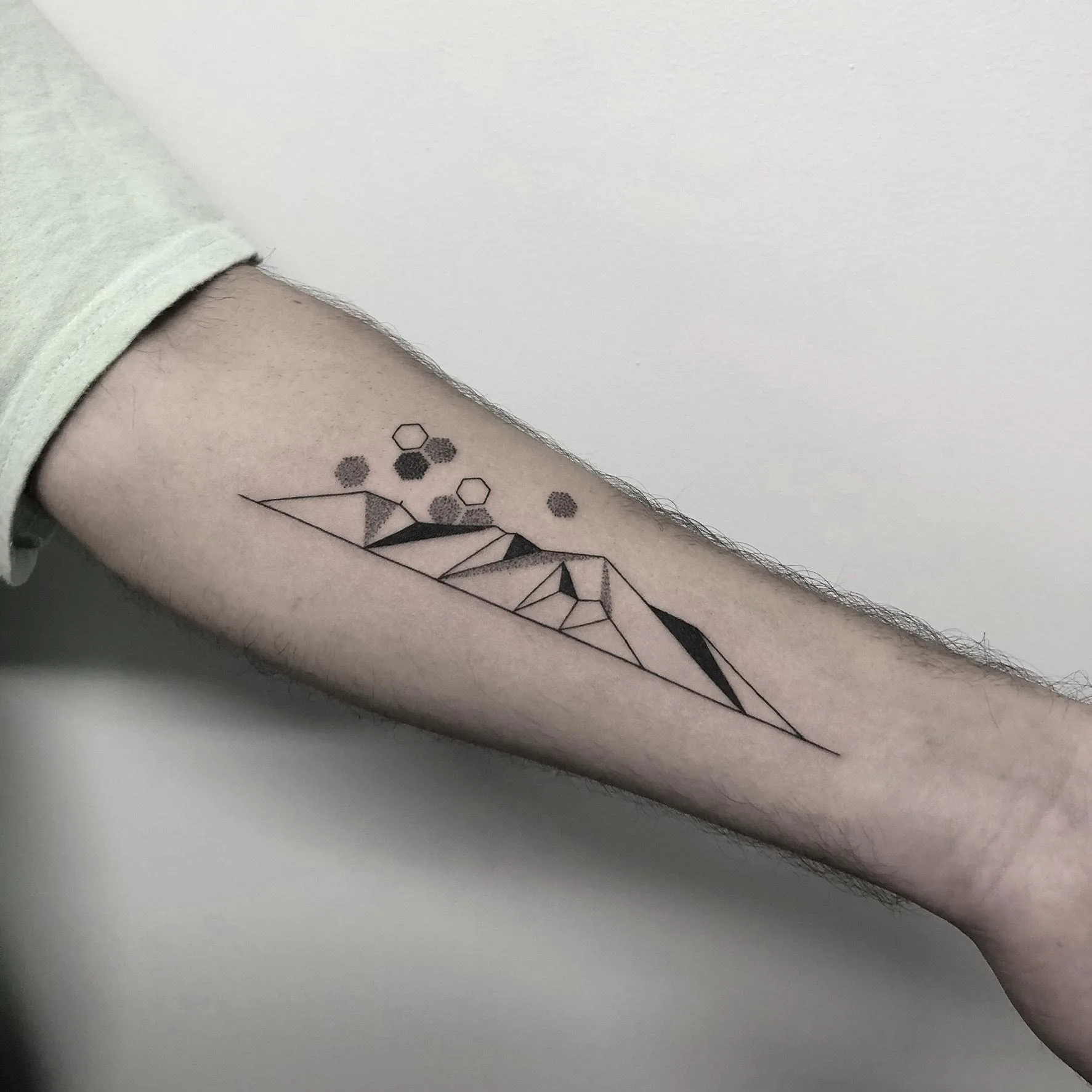 Tatuaje minimalista de montañas geométricas con hexágonos y sombreado en negro, estilo blackwork moderno.