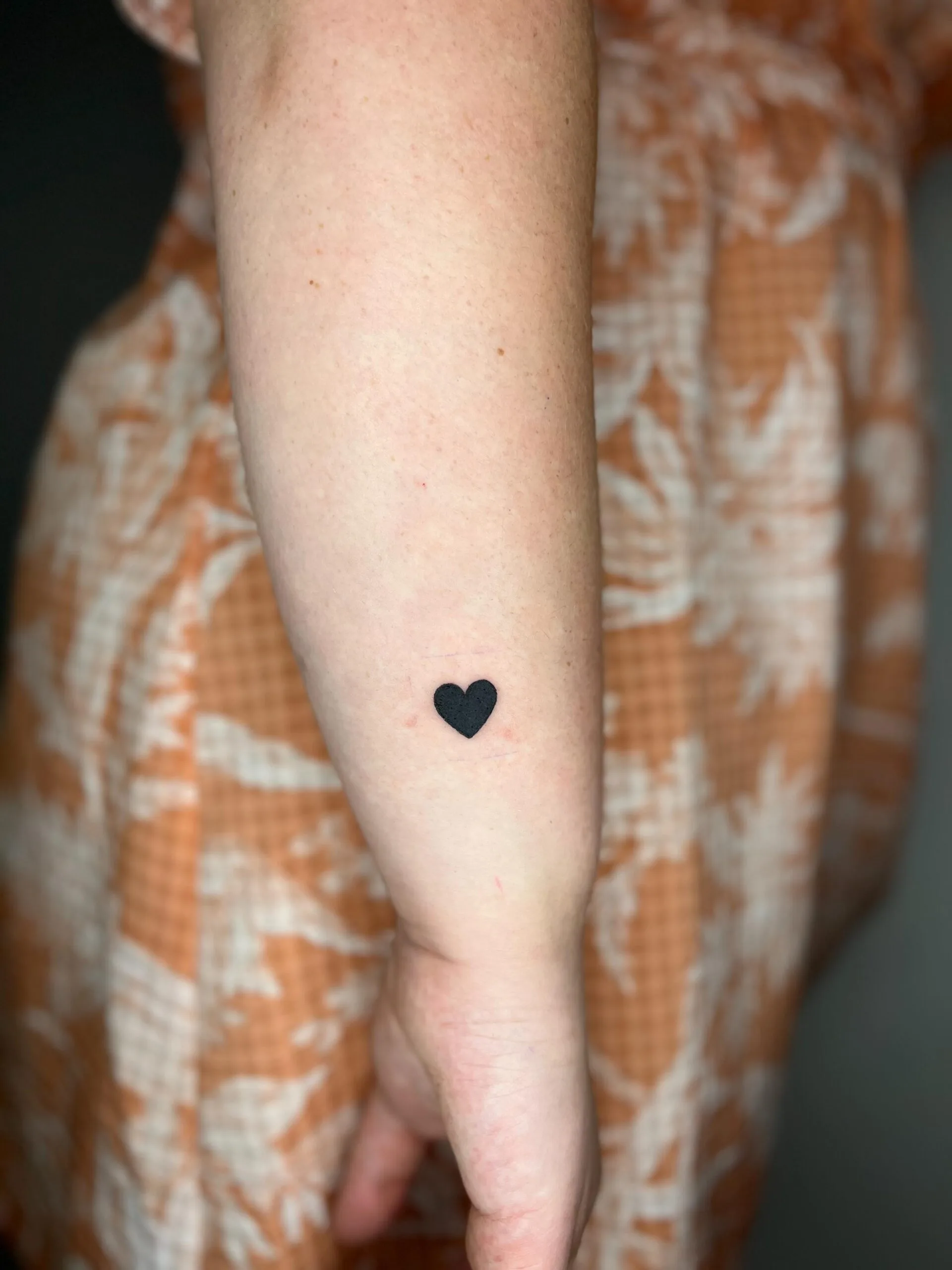 Tatuaje de un pequeño corazón negro sólido en el antebrazo, estilo minimalista y discreto.