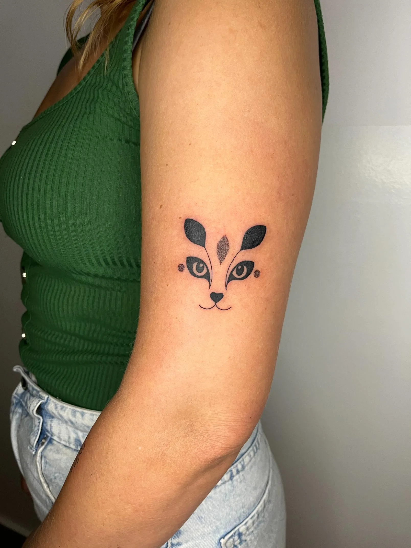 Tatuaje minimalista en el brazo de un rostro de zorro estilizado con formas geométricas negras.