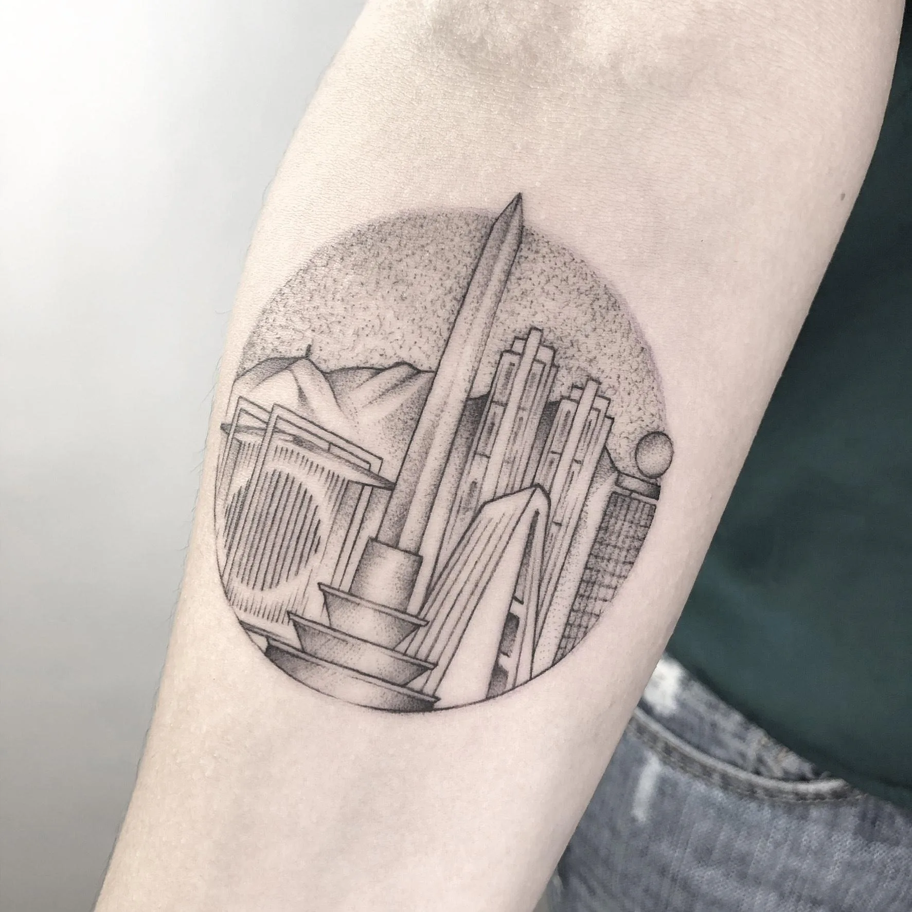 Tatuaje en estilo dotwork de un paisaje urbano, con elementos arquitectónicos y montañas en el fondo.