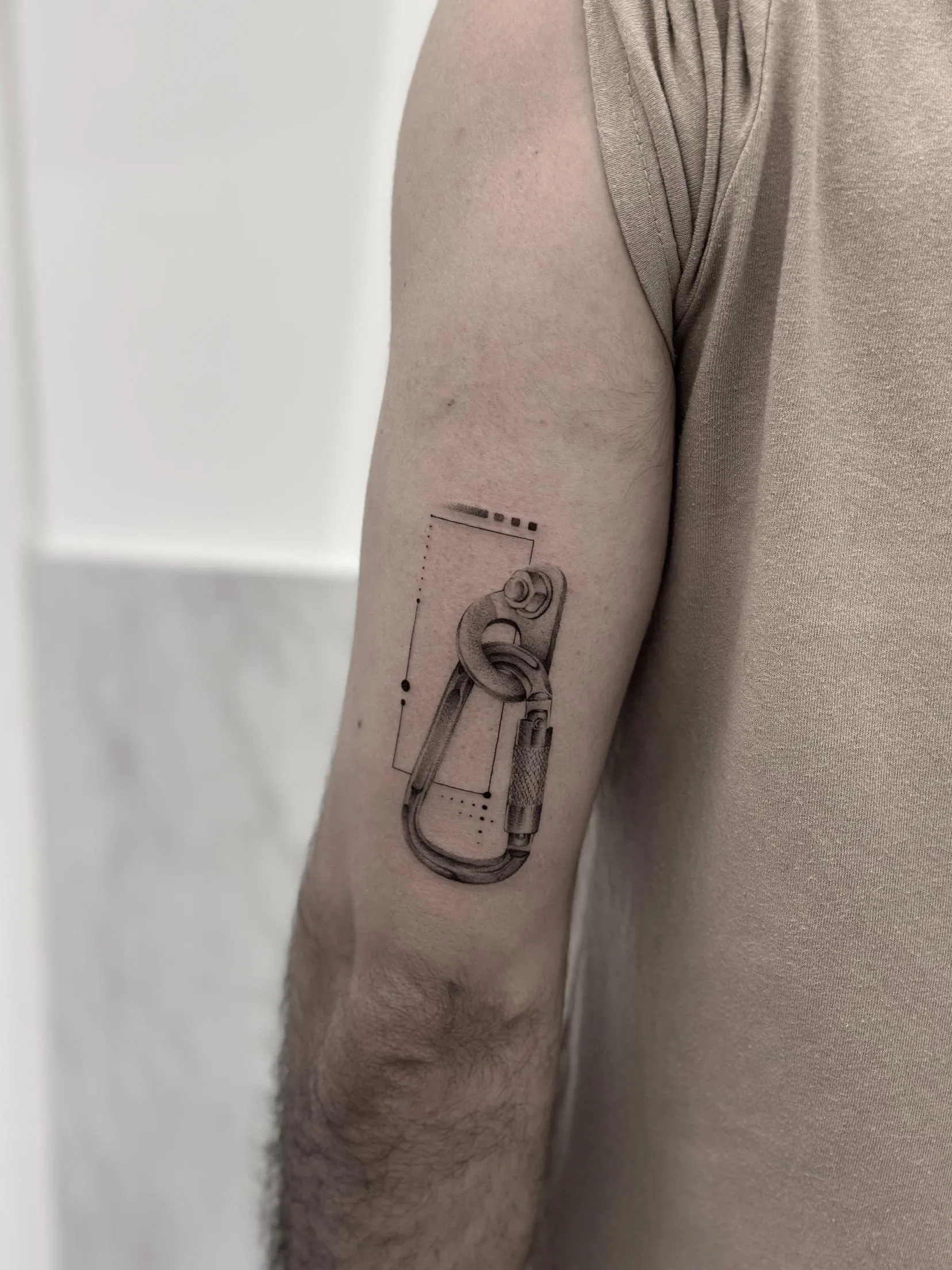 Tatuaje de un mosquetón en el brazo, estilo microrealismo con detalles precisos en el diseño.