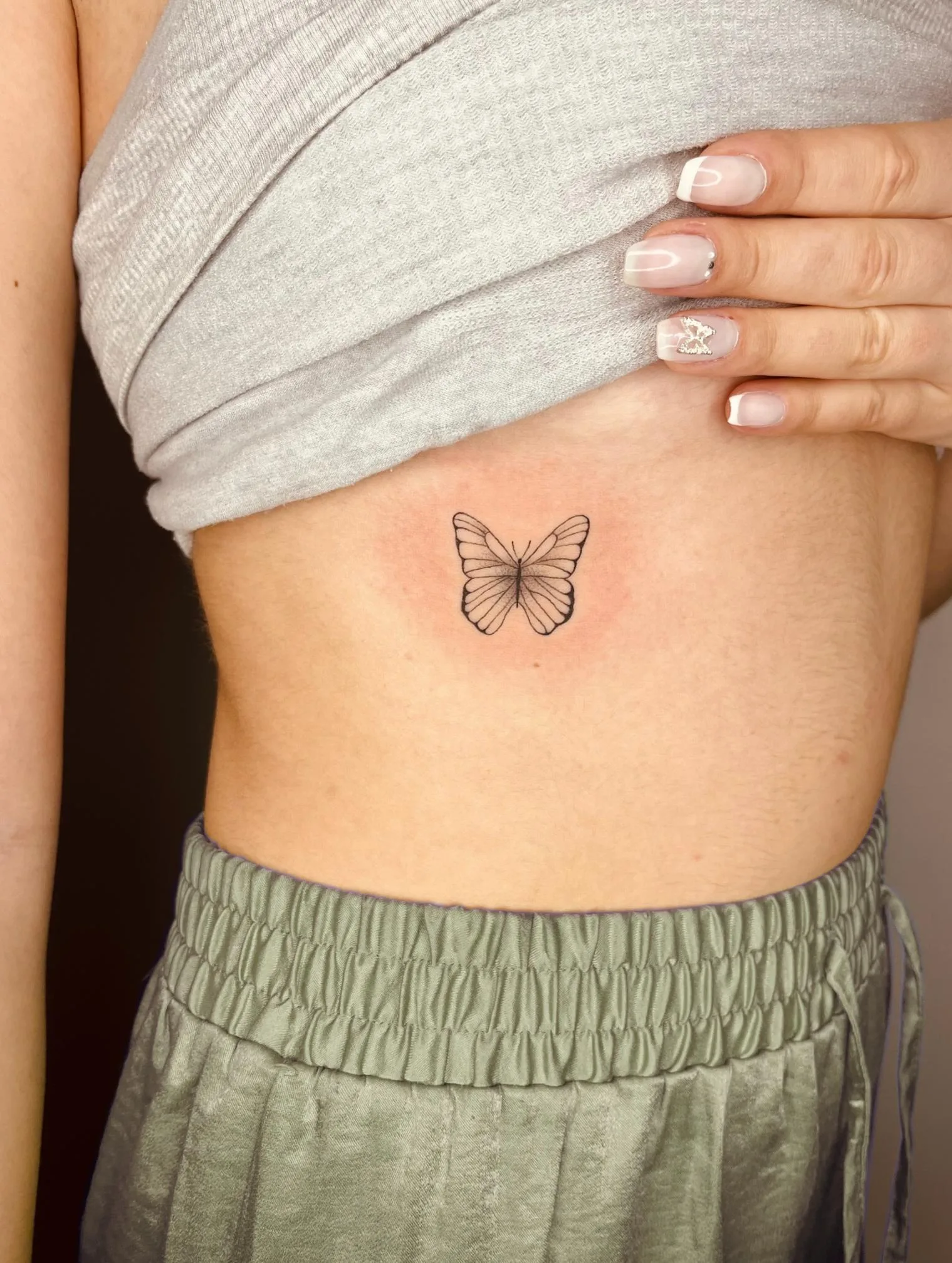 Tatuaje de una mariposa en el costado, estilo minimalista en tinta negra, con líneas finas en las alas.