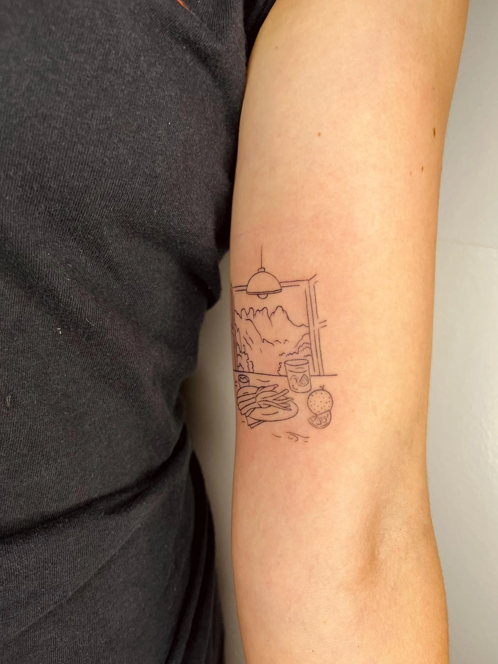 Tatuaje minimalista en el antebrazo, representando una escena de ventana con una vista al paisaje, comida y elementos de interior.