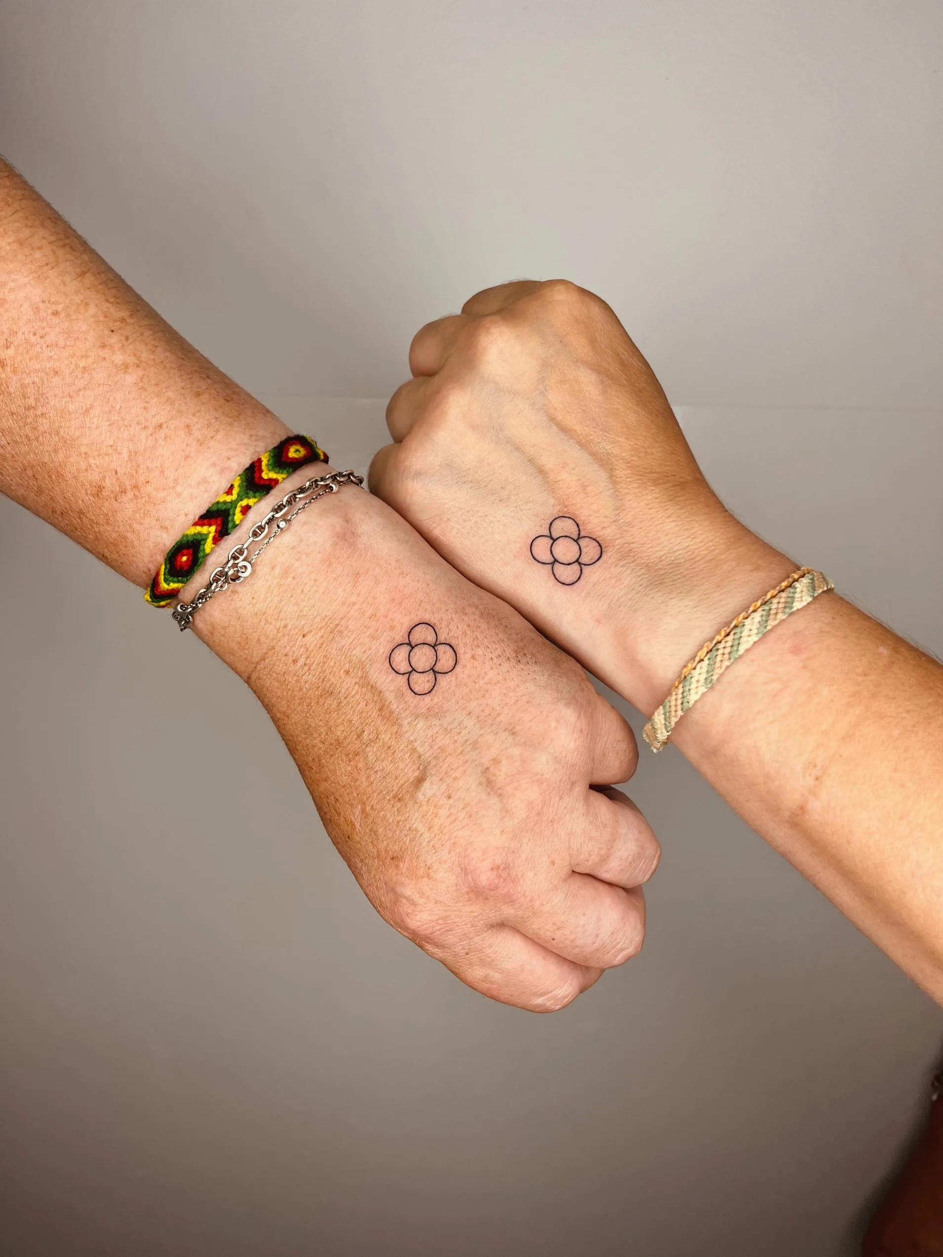 Tatuaje minimalista de parejas en el dorso de las manos, con pequeños círculos formando una figura floral en cada mano.