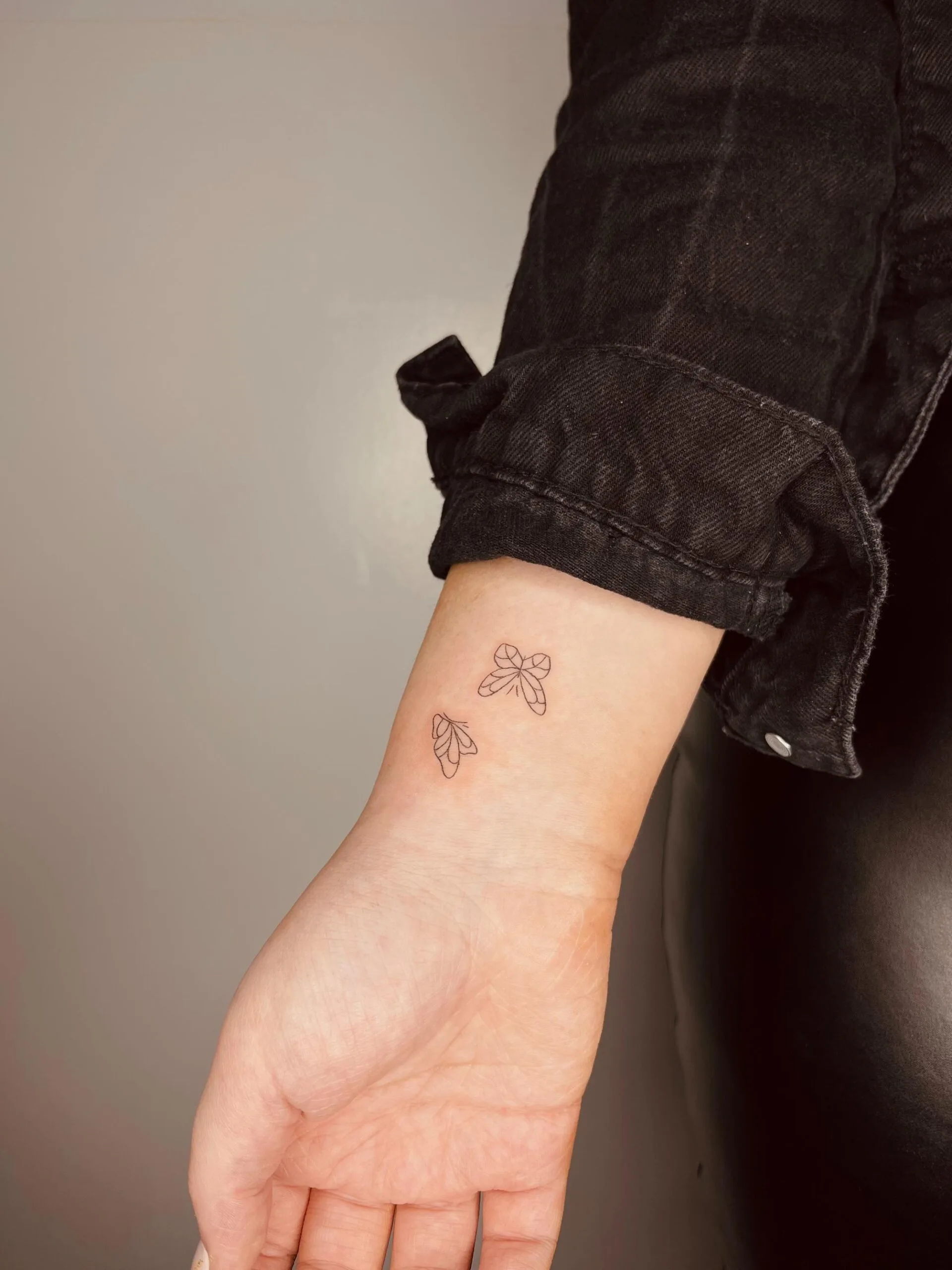 Tatuaje de estilo minimalista en la muñeca, con tres figuras de insectos en un diseño pequeño y delicado en tinta negra.