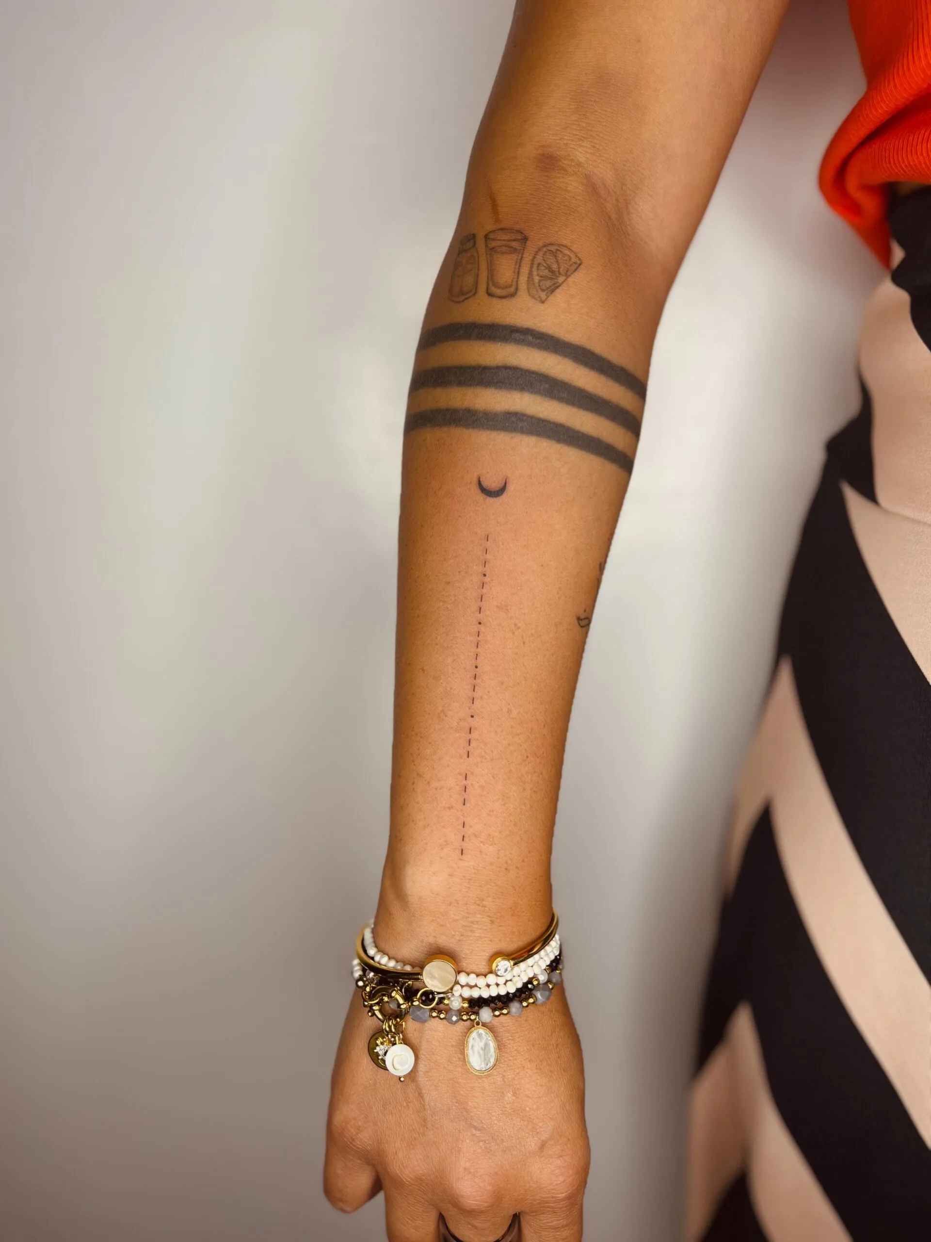 Tatuaje de estilo minimalista en el antebrazo, con una serie de líneas horizontales y una pequeña luna en el centro.