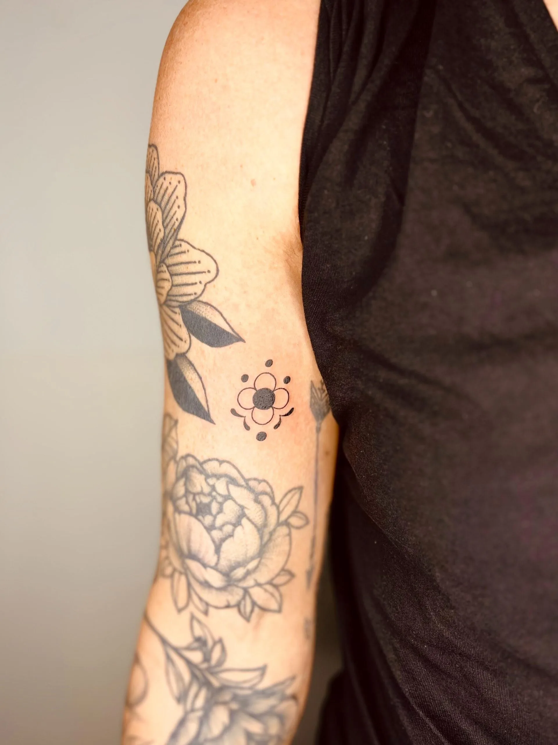 Tatuaje de estilo minimalista en el brazo, con un diseño floral de puntos y líneas finas en tinta negra.