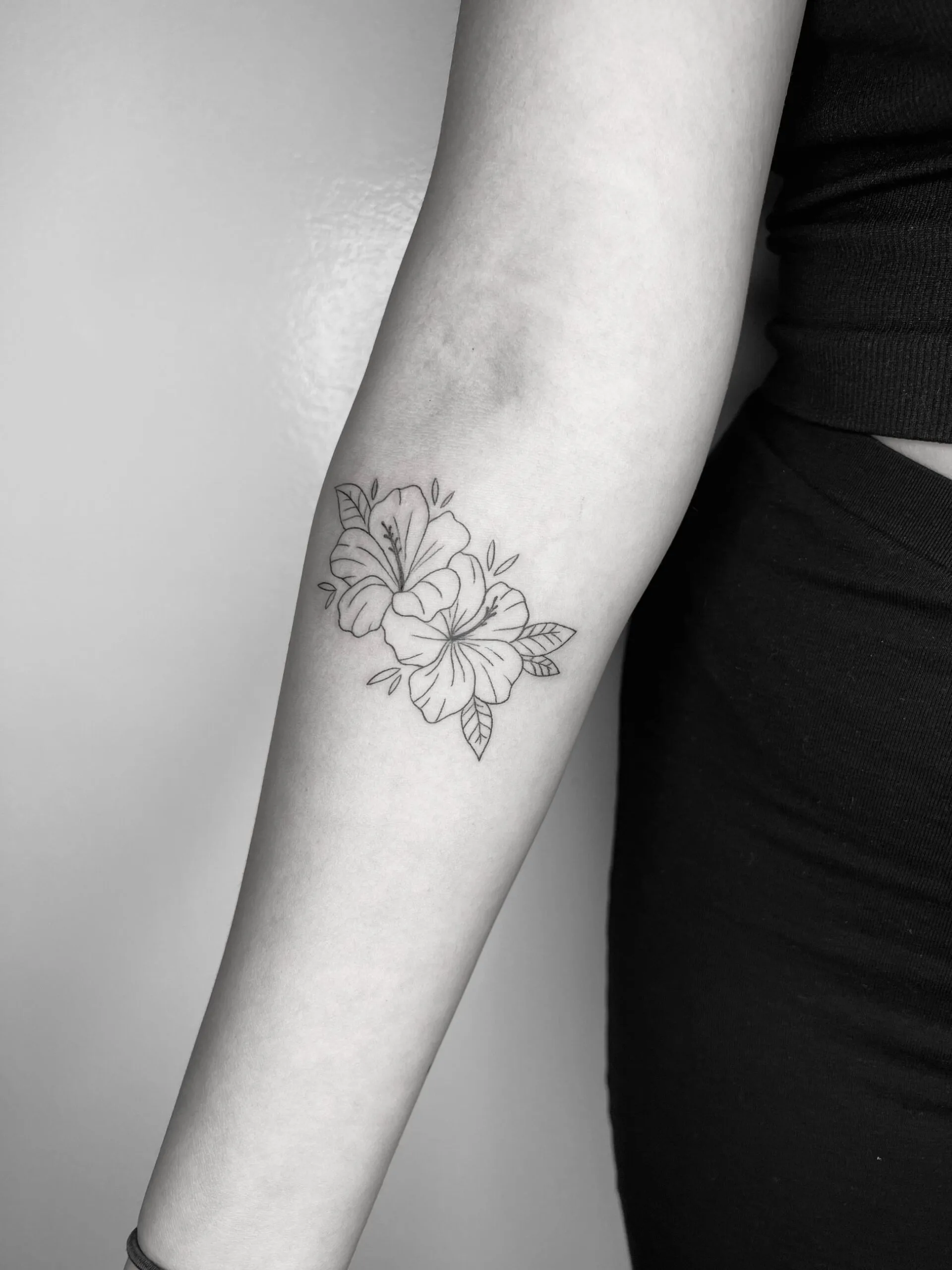 Tatuaje de flores estilo línea fina en el antebrazo, diseño minimalista y natural.