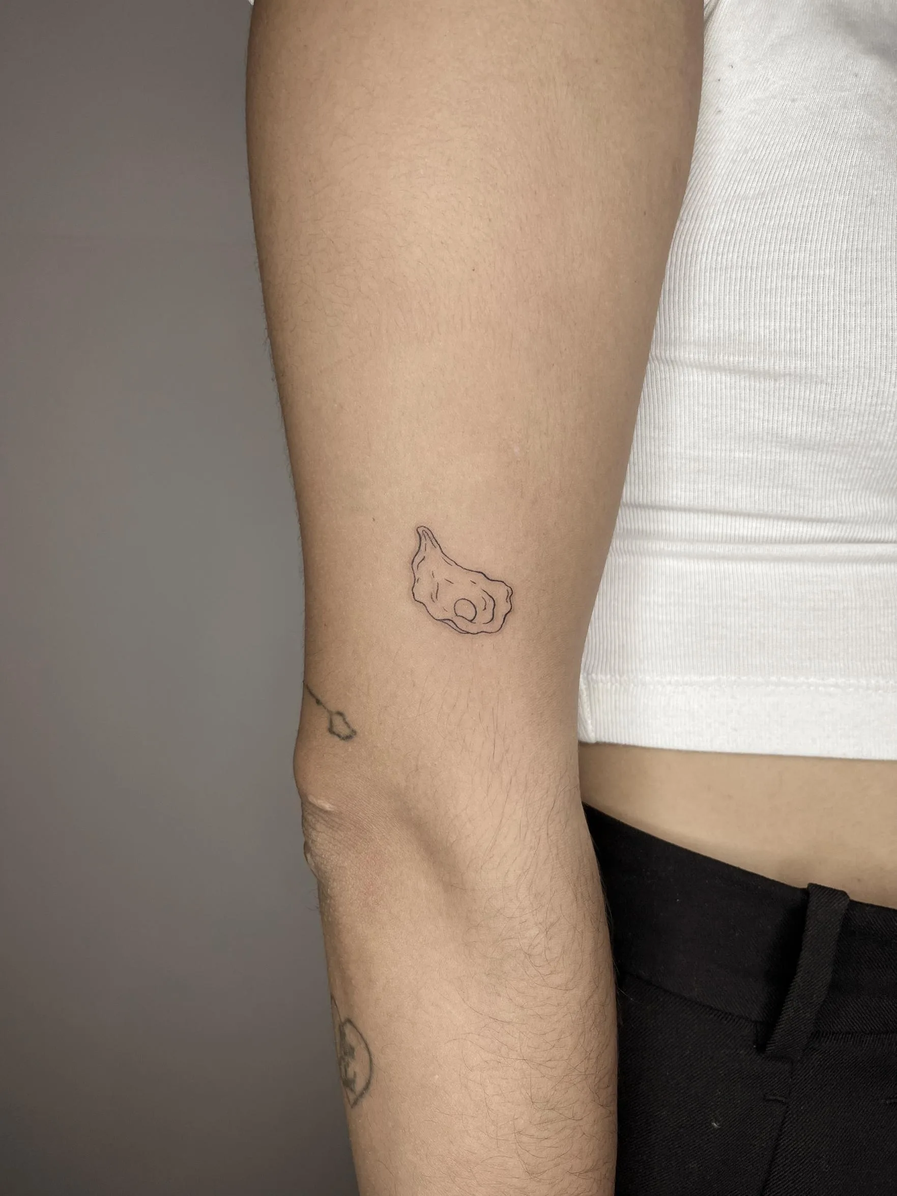Tatuaje minimalista en el brazo de un pequeño contorno de hueso, realizado con líneas finas y un estilo discreto y moderno.