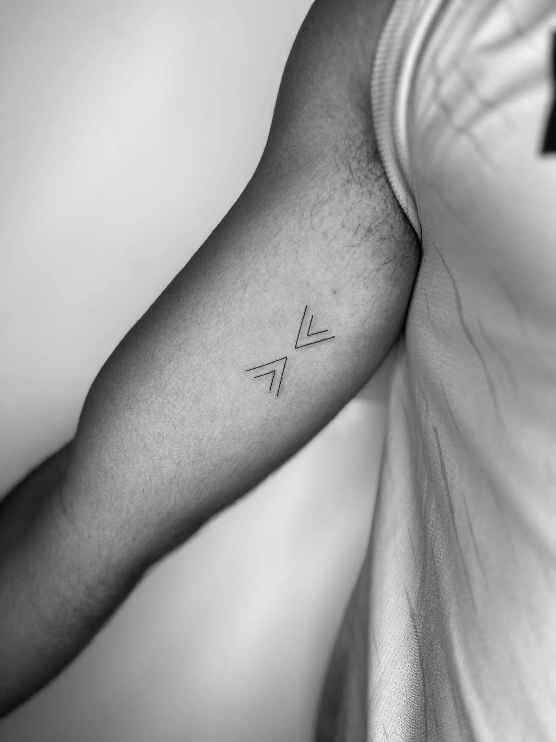 Tatuaje de dos flechas minimalistas apuntando hacia abajo en el brazo, realizado en líneas finas y simples.