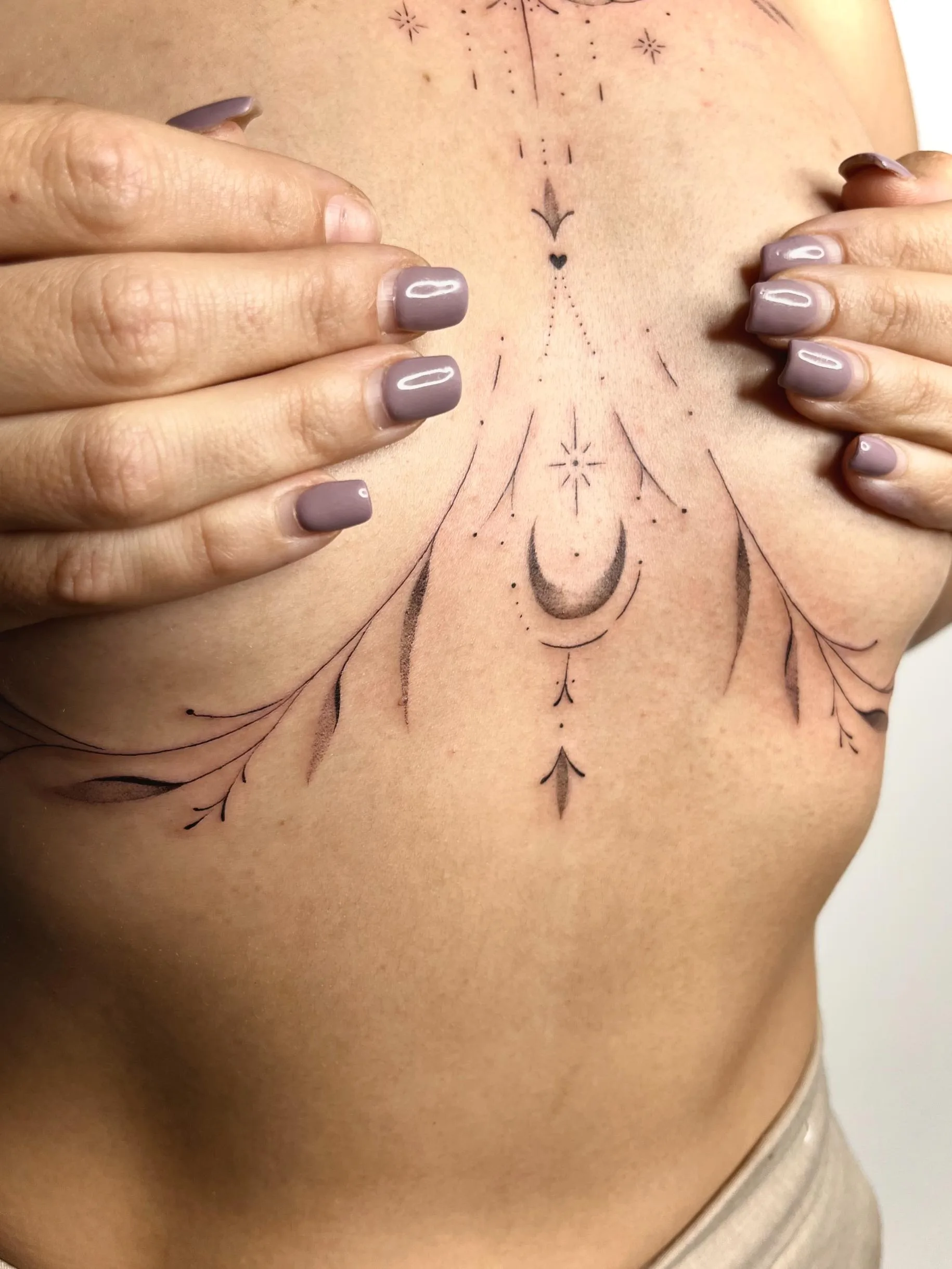 Tatuaje ornamental en el pecho, con un diseño simétrico de ramas, hojas, puntos y una media luna en el centro.